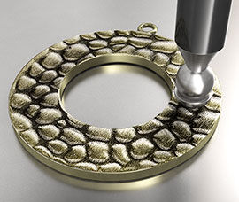 A round, textured metal ring being worked on with a dapping tool.